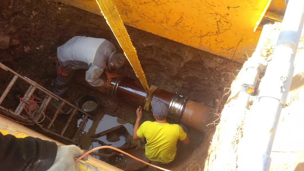 Monterzy osadzają segment rury w wykopie przy studzience
